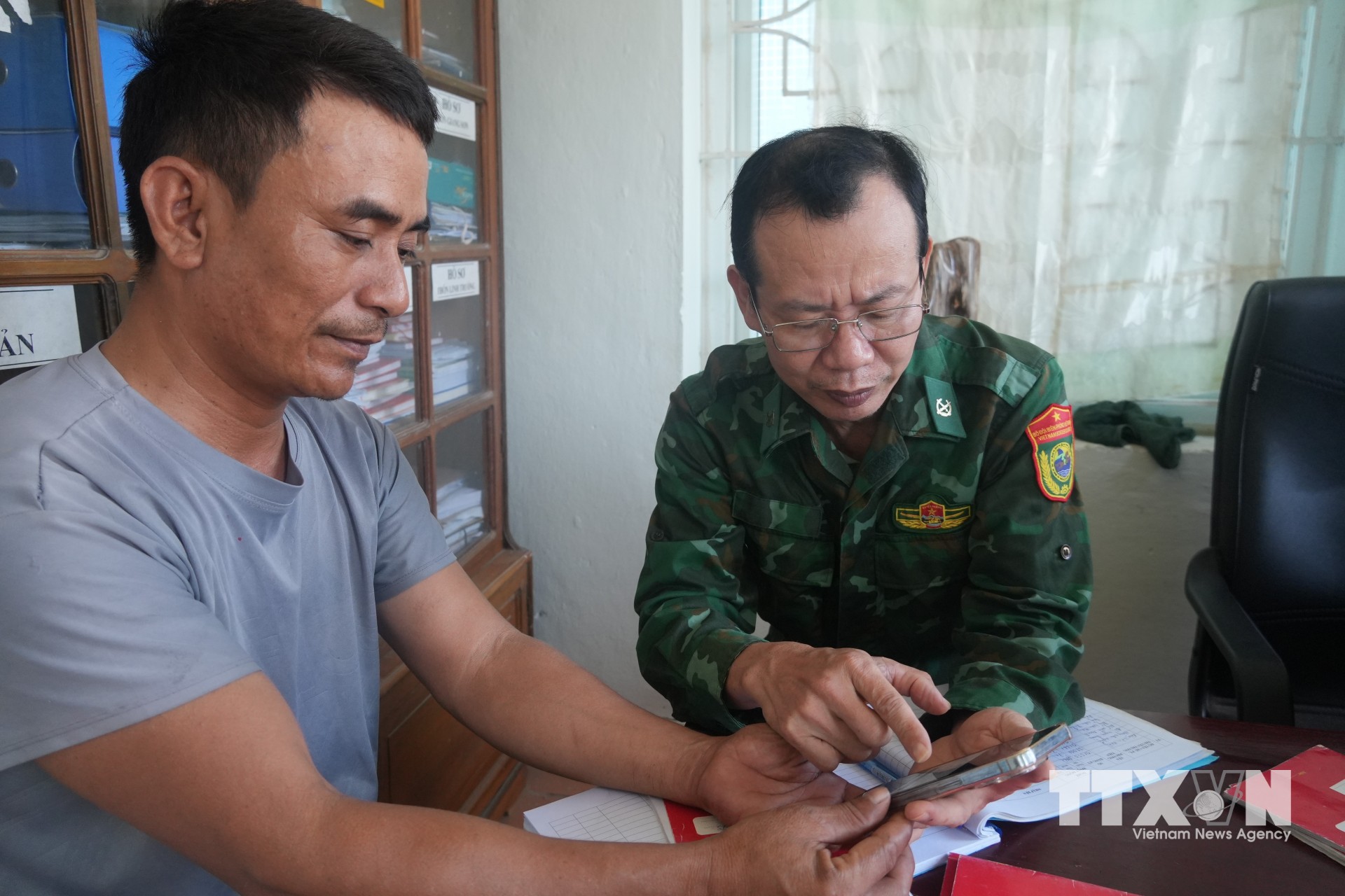 Anh Nguyễn Văn Hưng, chủ tàu TH-92543-TS, xã Hoa Lộc, tỉnh Thanh Hóa được cán bộ Biên phòng hướng dẫn sử dụng nhật ký điện tử và truy xuất nguồn gốc e-CDT trên điện thoại thông minh. (Ảnh: Hoa Mai/TTXVN)